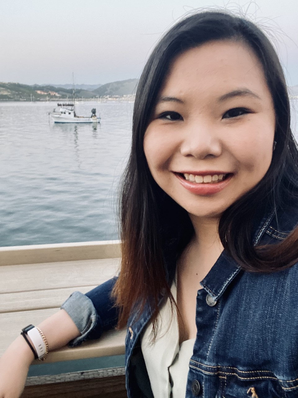 Photo of asian woman with dark hair, wearing a blue jean jacket, with a body of water in the background