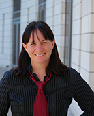 Photo of white woman with dark hair wearing a black shirt and red tie
